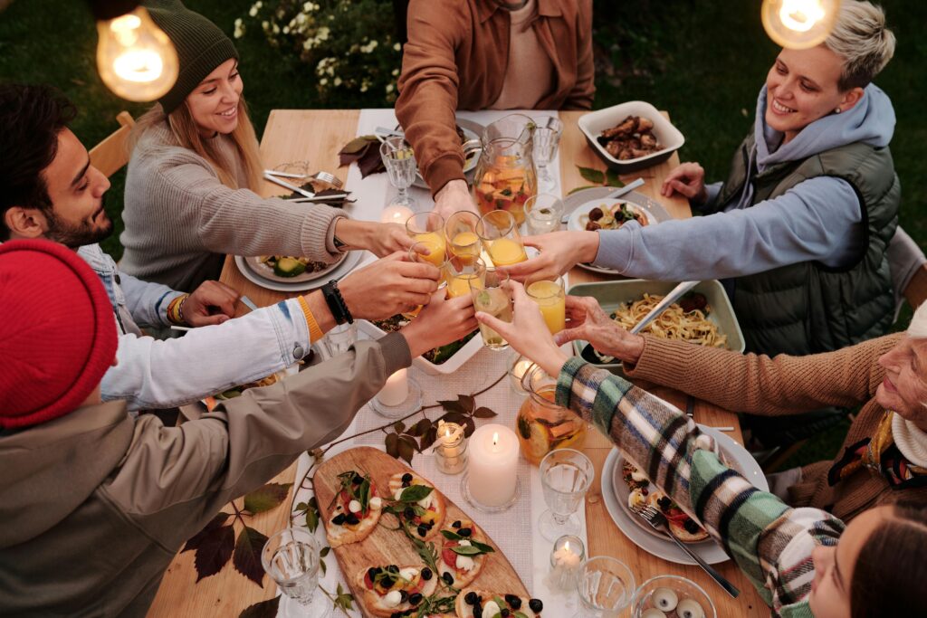 Group of friends toasting with glasses at an outdoor dinner table. Lively and joyful atmosphere.