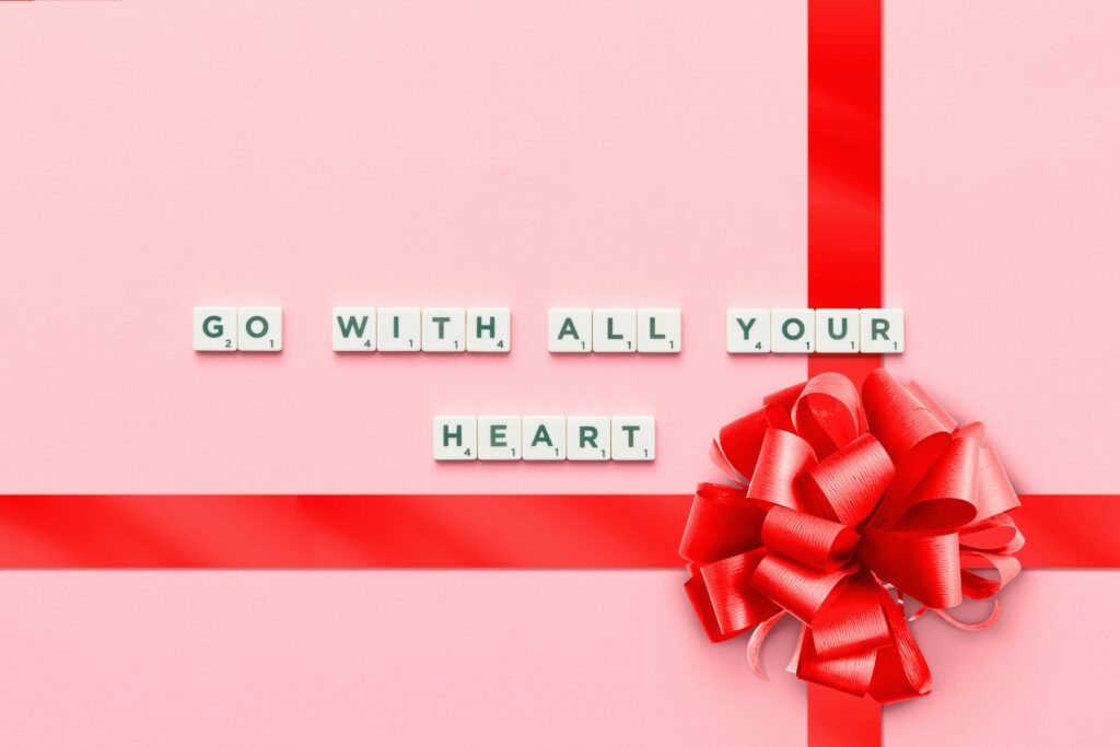 Pink gift box with red ribbon and 'Go With All Your Heart' spelled out, inspiring mood.