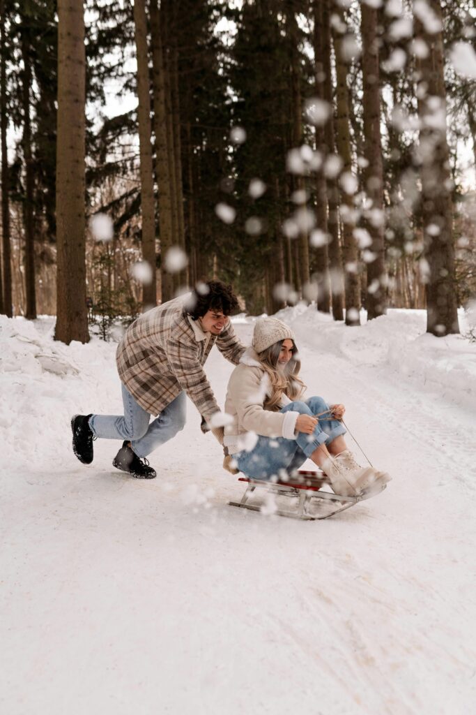 A couple enjoys a playful sled ride through a snowy forest, capturing winter fun.