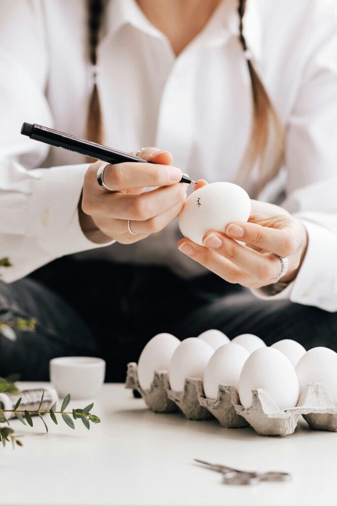 Person decorating Easter eggs with a marker, sitting indoors.